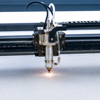 Laser cutting head cutting a filter panel, the beam glowing at the fabric surface