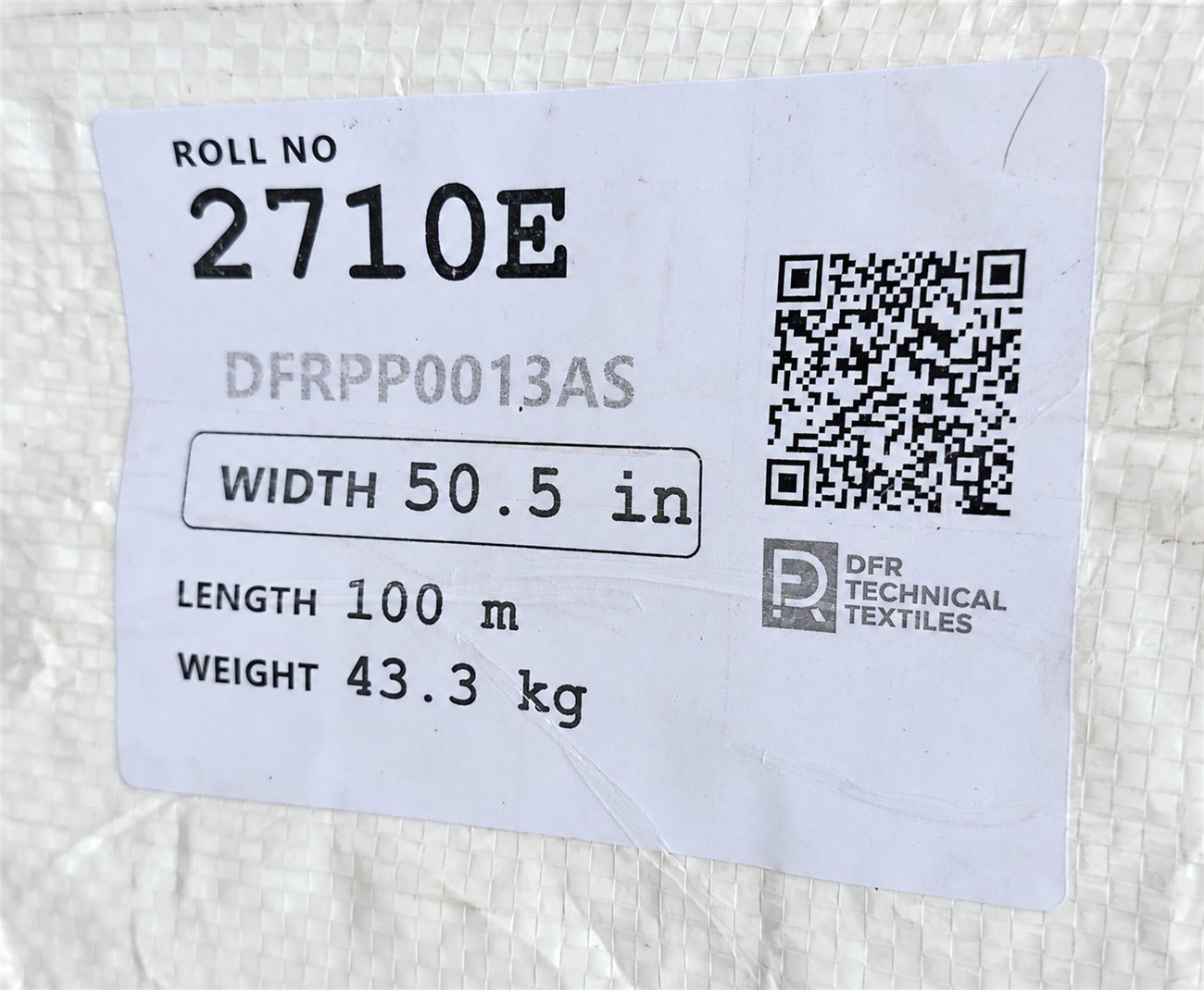 Printed label on a wrapped roll of DFR filtration fabric, showing roll number 2710E, the article code, width 50.5 inches, length 100 metres, weight 43.3 kilograms and a QR code